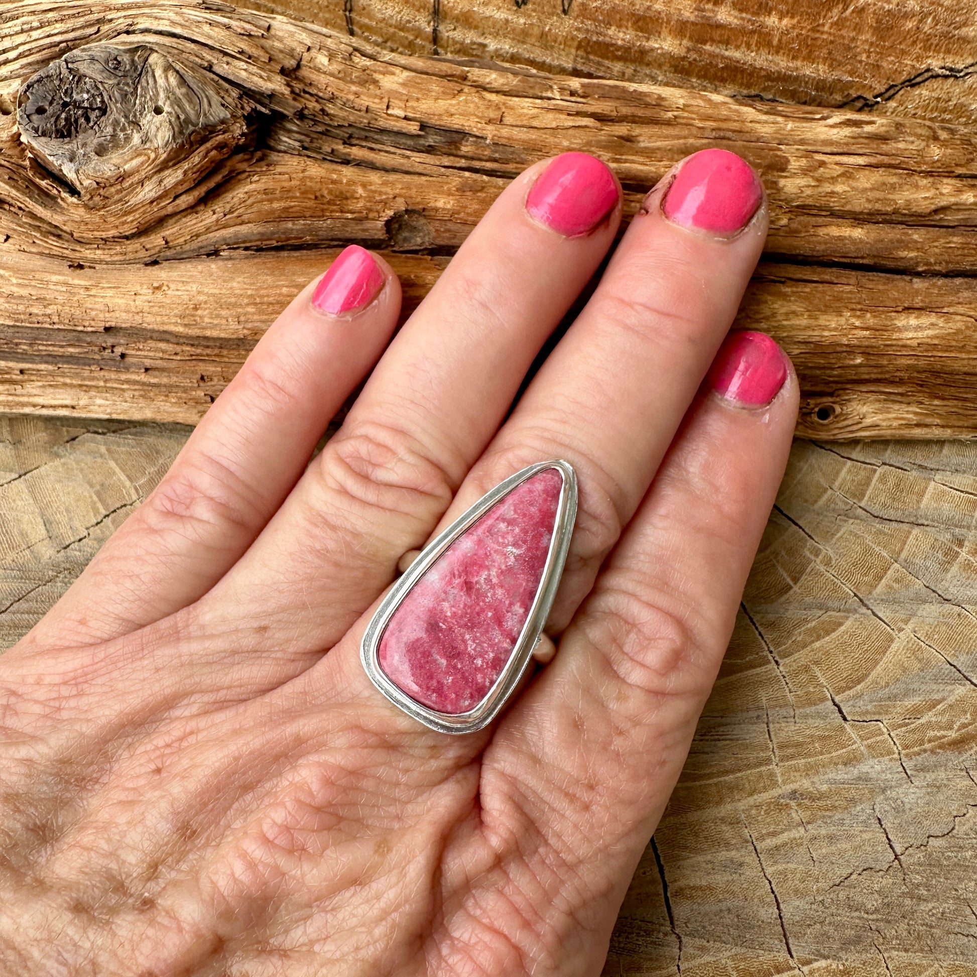 Hand wearing a pink stone ring on a wooden surface